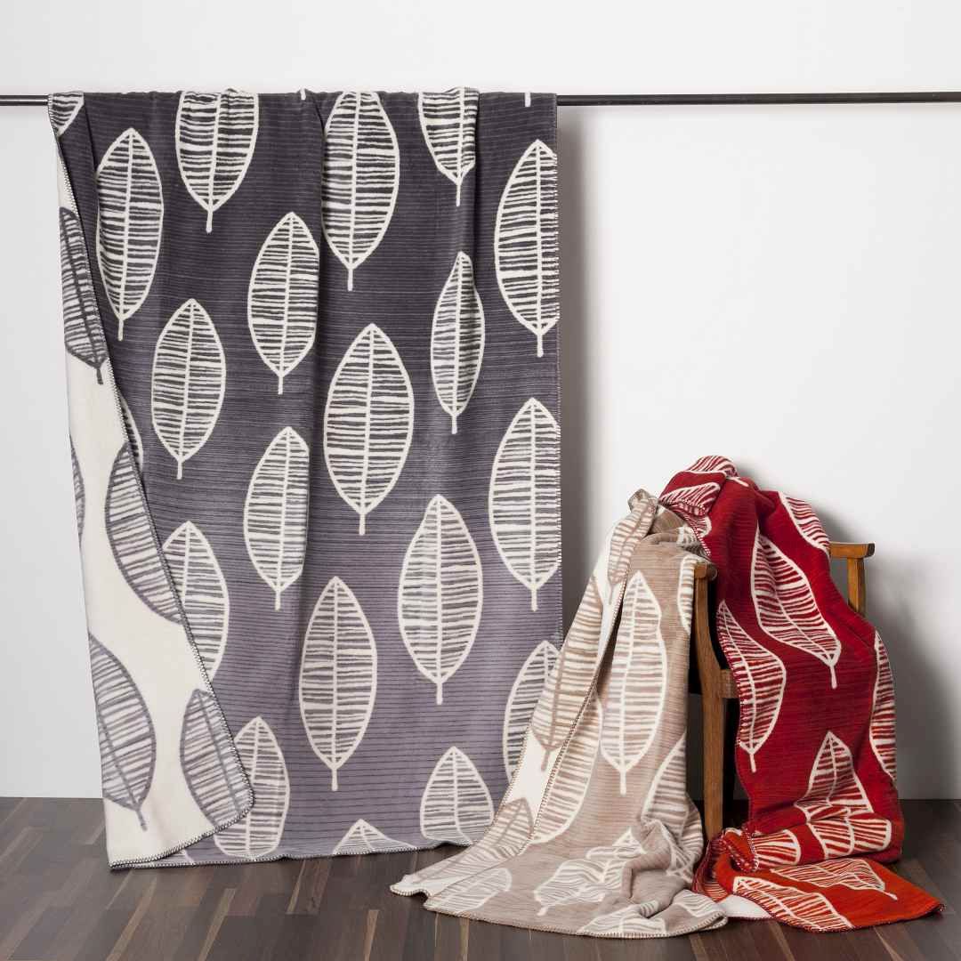 Nachhaltige Wohndecken aus Bio Baumwolle sind drei Bio Wohndecken abgebildet. Eine ist grau, eine beige und eine rot. Sie sind nachhaltig aus Bio Baumwolle